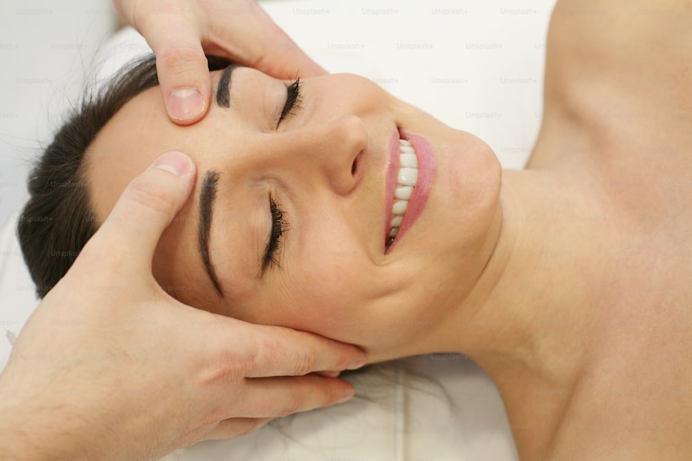 Esteticista feminina massageando cabeça e rosto de mulher jovem durante o tratamento facial.