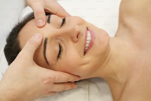 Estetista femminile che massaggia la testa e il viso della giovane donna durante il viso.