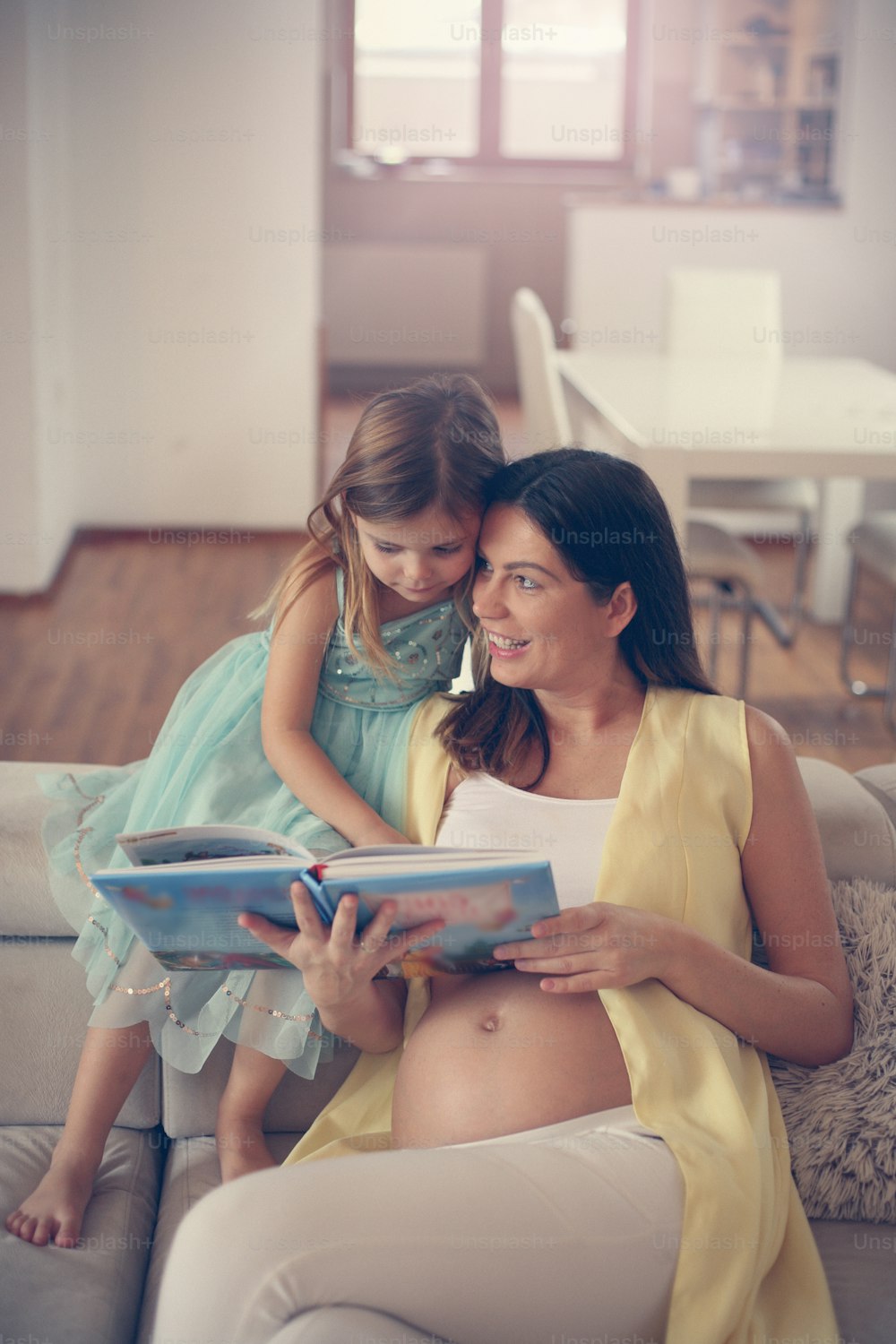 Young pregnant woman reading book her daughter.