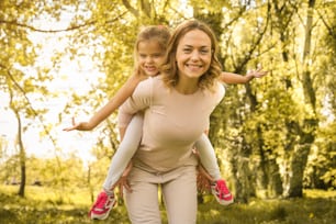 Mother and daughter outdoors in a meadow. Mother carrying her daughter on piggyback.