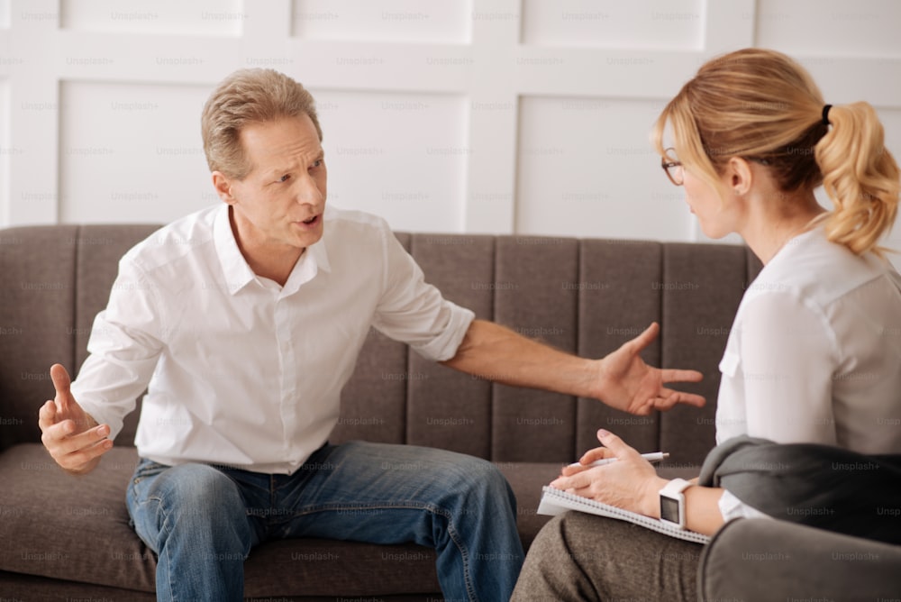 Emociones negativas. Hombre infeliz enojado emocional que mira a su psicólogo y se queja de sus problemas mientras busca consejo