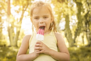 Little girl eating ice-cream. Blonde little girl enjoying in beautiful spring day. Looking at camera.