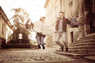 Couple holding shopping bags and jumping outdoor.