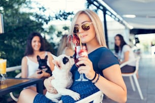 Beautiful young woman sitting in cafe with her adorable French bulldog puppy. Spring or summer city outdoors. People with dogs theme.