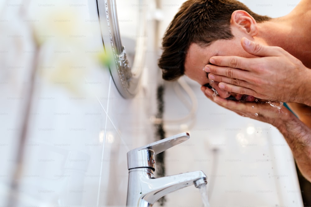 Homem lavando o rosto pela manhã e praticando a higiene