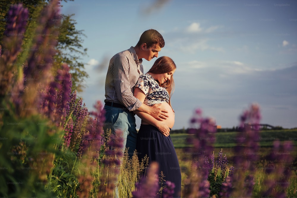 Happy beautiful girl pregnant with her husband outdoors on a background of flowers