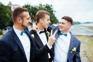 Beau marié souriant confiant en costume noir avec deux garçons d’honneur
