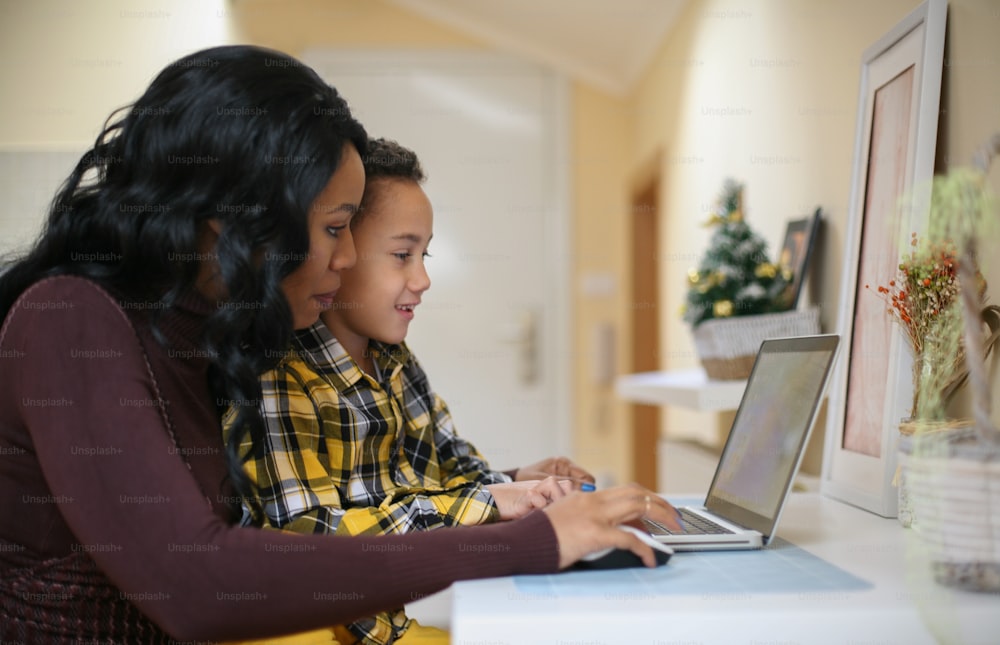 Una mujer afroamericana y su hijo usando una computadora portátil en casa.