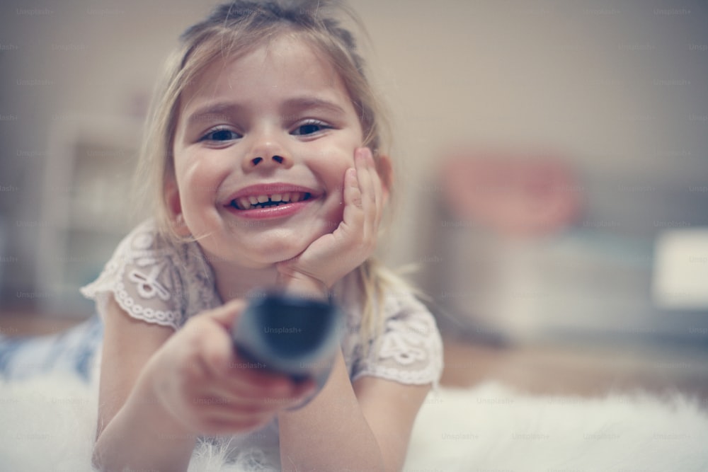 Little girl watching TV lying on floor with remote control in hand.