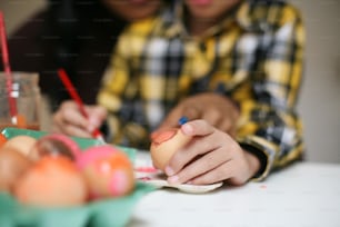 Close up de mulher afro-americana e seu filho decorando ovo para a Páscoa. Foco nas mãos.