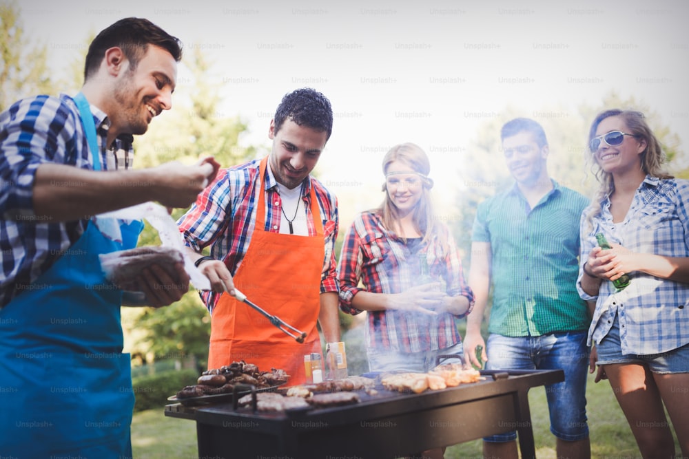 Happy friends grilling meat and enjoying barbecue party outdoors