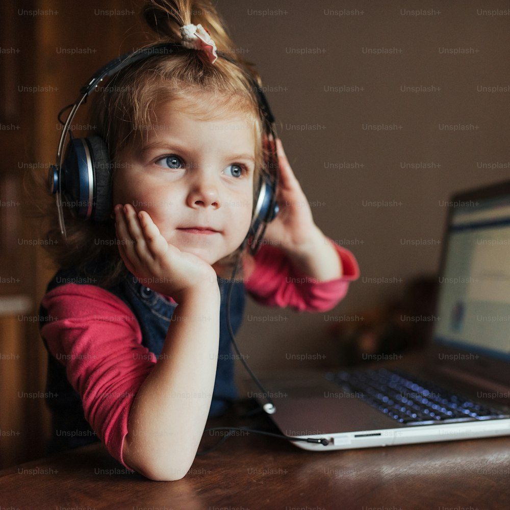 little girl with headphones listening to music, using laptop.