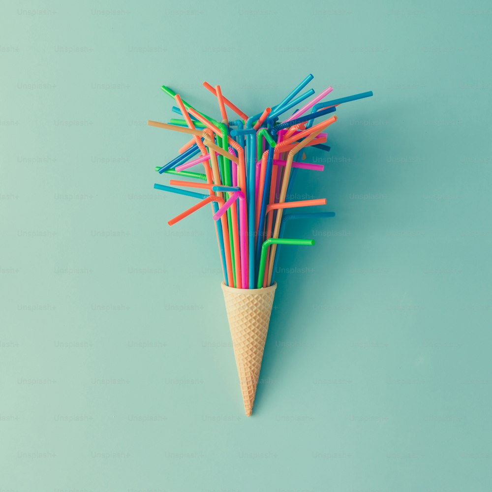 Ice cream cone with colorful drinking straws on bright blue background. Minimal food concept. Flat lay.