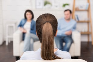 Psicologia do casal e da família. Profissional simpática psicóloga sentada em frente a seus pacientes e olhando para eles enquanto tem uma sessão psicológica