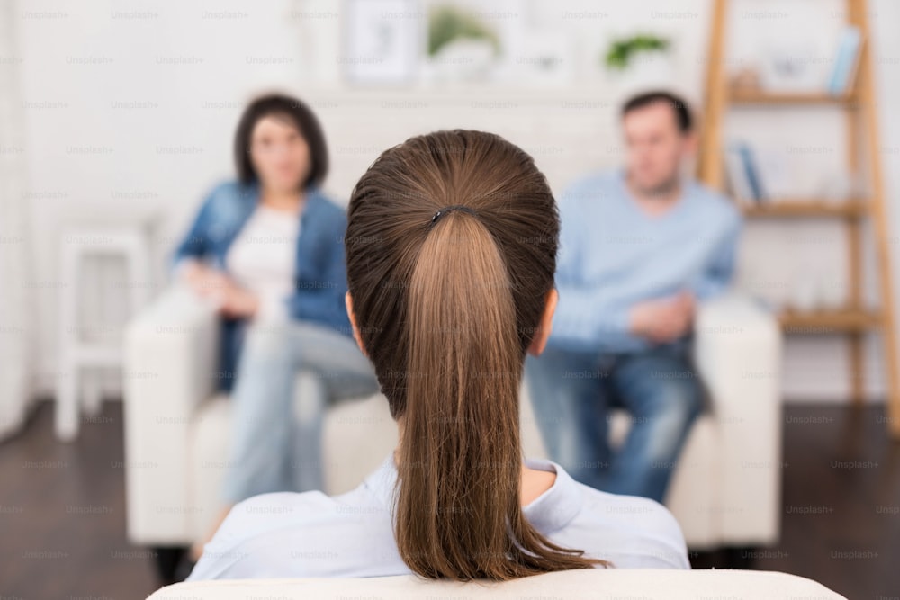 Couple and family psychology. Professional nice female psychologist sitting opposite her patients and looking at them while having a psychological session