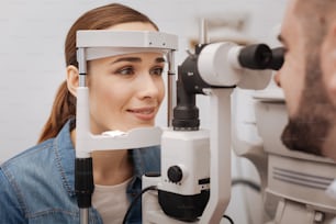 Examen médical. Belle femme attrayante et agréable posant sa tête sur un appareil spécial et vérifiant sa vue lors d’une visite chez un ophtalmologiste