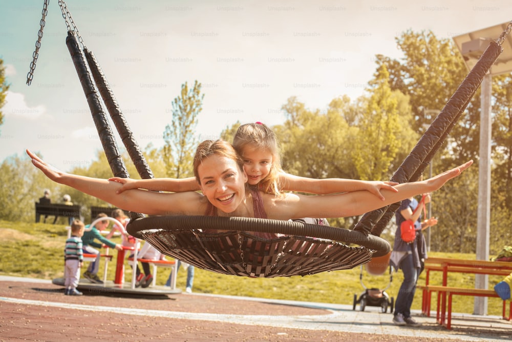 Mother and daughter playing on the swing. Looking at camera.