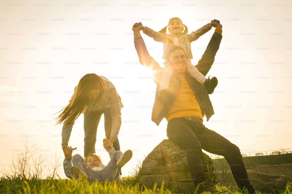 Parents play with his daughters in the park. Daughter sitting on father shoulders. Looking at camera.