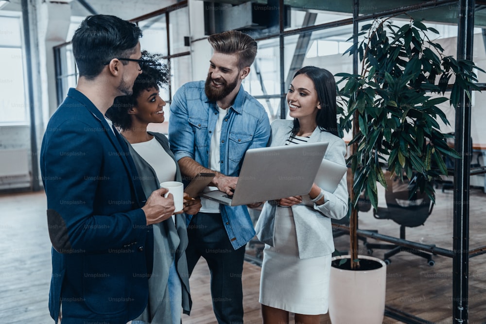 Group of young business people in smart casual wear talking and smiling while standing in the office hallway