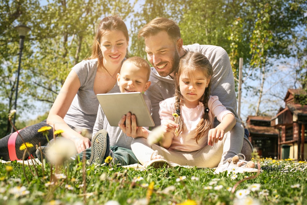 Happy family using tablet outdoors, sitting on the green grass.