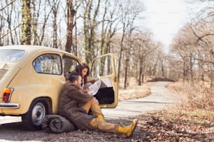 恋をしている若いカップルがロードトリップで休憩し、道路脇に座って地図を見ながら、ルートを決めようとしています