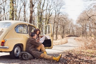 Young couple in love taking a break on their road trip, sitting by the road and looking at a map, trying to decide their route