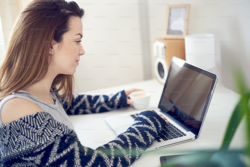 Beautiful Caucasian girl sitting in living room and using laptop in the morning