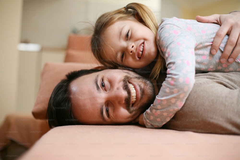 Father with his daughter spending time at home. Little girl looking at camera.