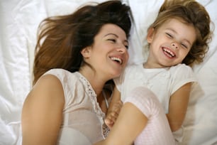 Mother with her cute little daughter sitting  on bed. "nEnjoy together in free time.