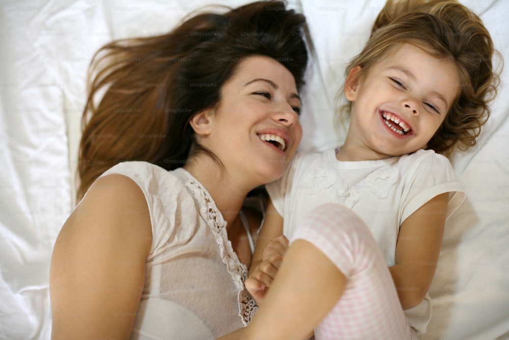 Madre con su linda hijita sentada en la cama. "Disfruten juntos en el tiempo libre.
