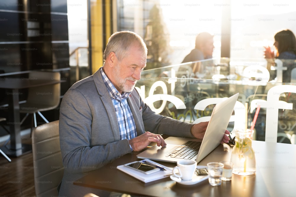 Bel homme d’affaires senior travaillant sur un ordinateur portable dans un café. Journée ensoleillée de printemps.