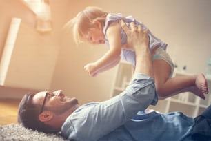 Padre feliz jugando con su hija. Padre tumbado en el suelo y disfrutando en el tiempo libre con su bebé.