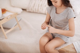 Full of independence. Concentrated skilled little girl sitting in the white colored room and putting band aid on her finger while enjoying medicine