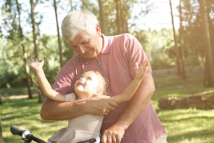 Senior man with granddaughter in bicycle basket, portrait.