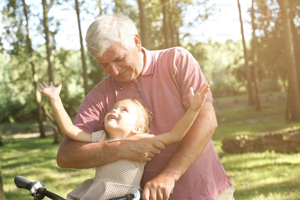 Senior man with granddaughter in bicycle basket, portrait.