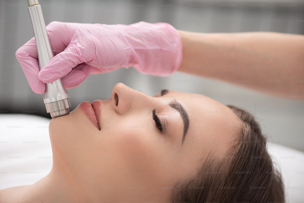 Close up profile of relaxed young woman is enjoying microdermabrasion treatment at cosmetology center. She is lying with closed eyes