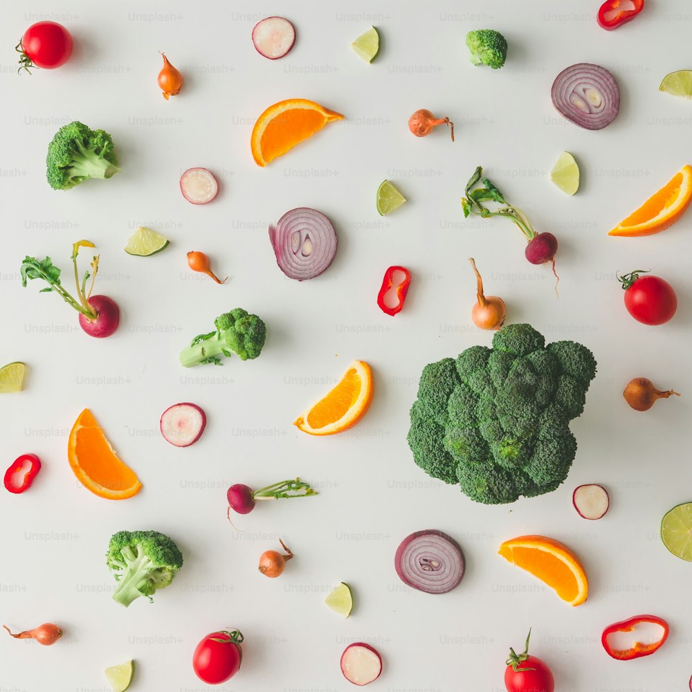 Motif alimentaire coloré à base de brocoli, d’orange, de poivron rouge, d’oignon, de tomates et de citron vert. Pose à plat.