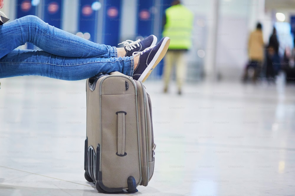 Gros plan des pieds d’une femme sur une valise dans un aéroport international. Concept de vol retardé ou annulé
