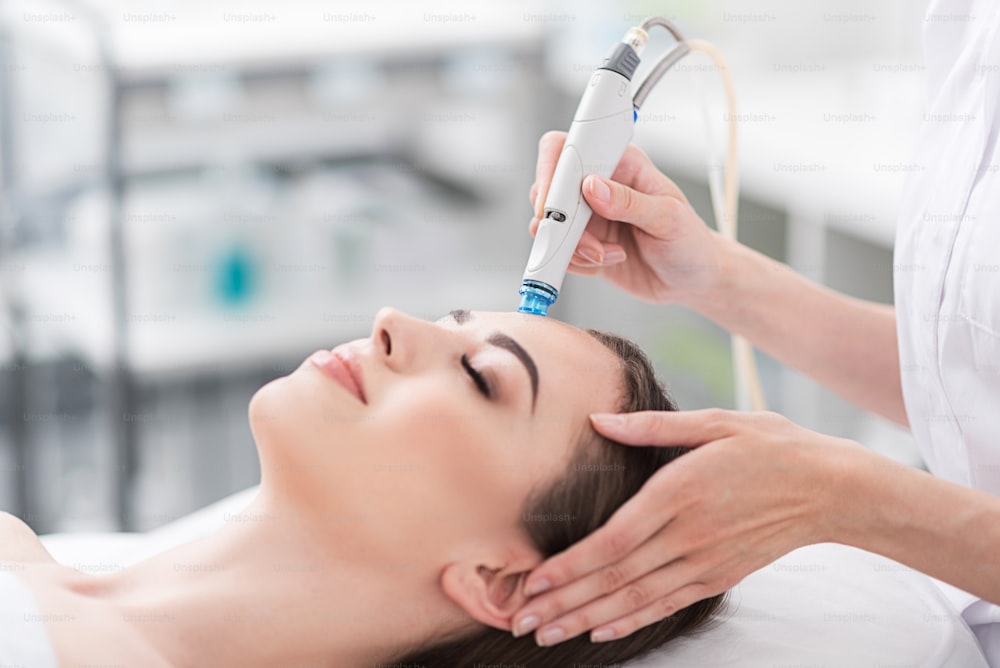 Face skin care. Close-up of young woman is getting facial hydro vacuum microdermabrasion peeling treatment at beauty shop. Focus on instrument