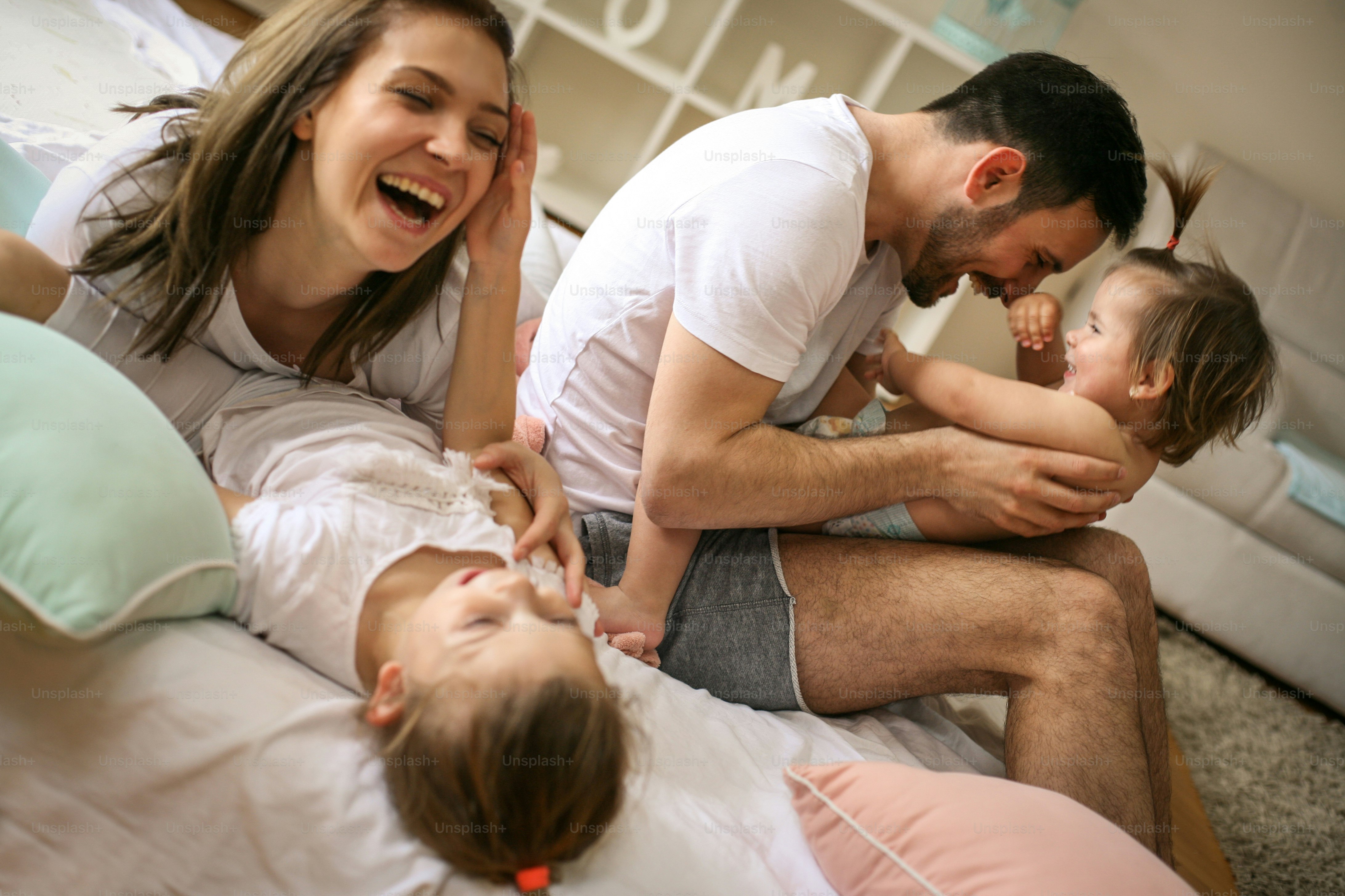 Family spending free time at home. Cheerful family having fun with their daughters on the bed.