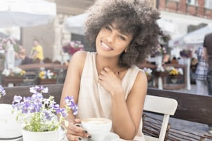 Hermosa joven afroamericana bebiendo café en el café, día soleado.