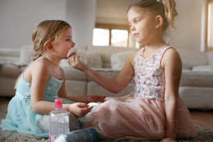 Little girl cleaning face of her small sister at home.