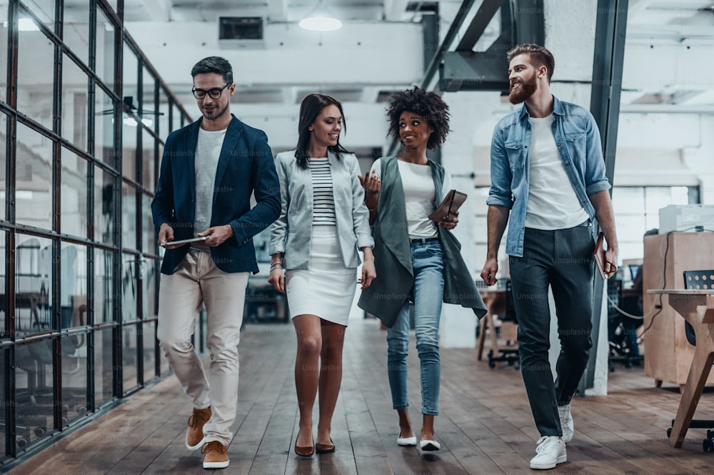 In voller Länge diskutieren junge moderne Menschen in eleganter Freizeitkleidung über Geschäfte, während sie durch den Bürokorridor gehen