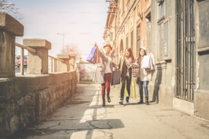 Drei beste Freunde gehen auf der Straße. Junges Mädchen zeigt einer Freundin ein neues Bekleidungsgeschäft
