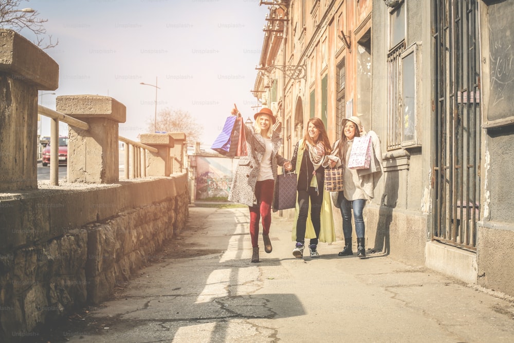 Three best friends walking on the street . Young girl showing a friends new clothing store