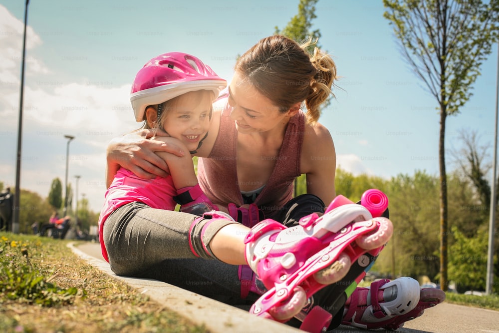 Smiling mother with her little daughter sitting on road after skating.