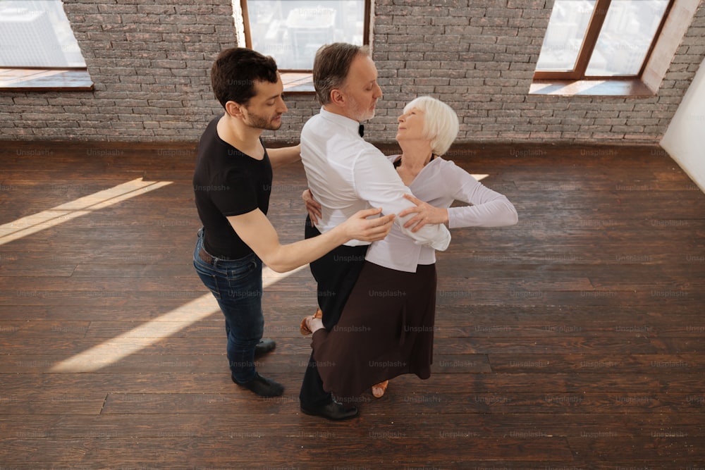 Praticando tango juntos. Sofá de dança atlético cuidadoso ensinando tango a aposentados idosos enquanto tem sessão de treinamento e expressa cuidado