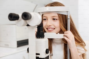 Following instructions. Yung pretty bright child paying a visit to her ophthalmologist and having her eyesight tested using special machinery