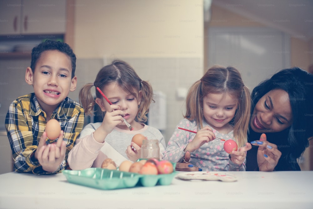 African American woman with three child prepare for Easter. Little boy looking at camera and holding egg.