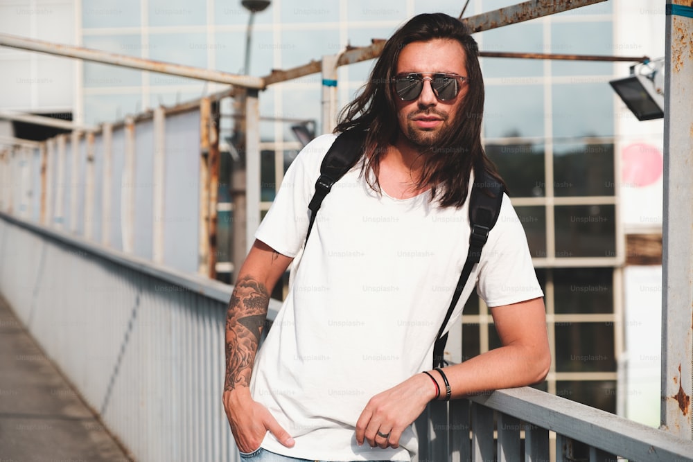 Stylish hipster model with long hair lifestyle in the street. Dressed in a white T-shirt and torn blue jeans in the city